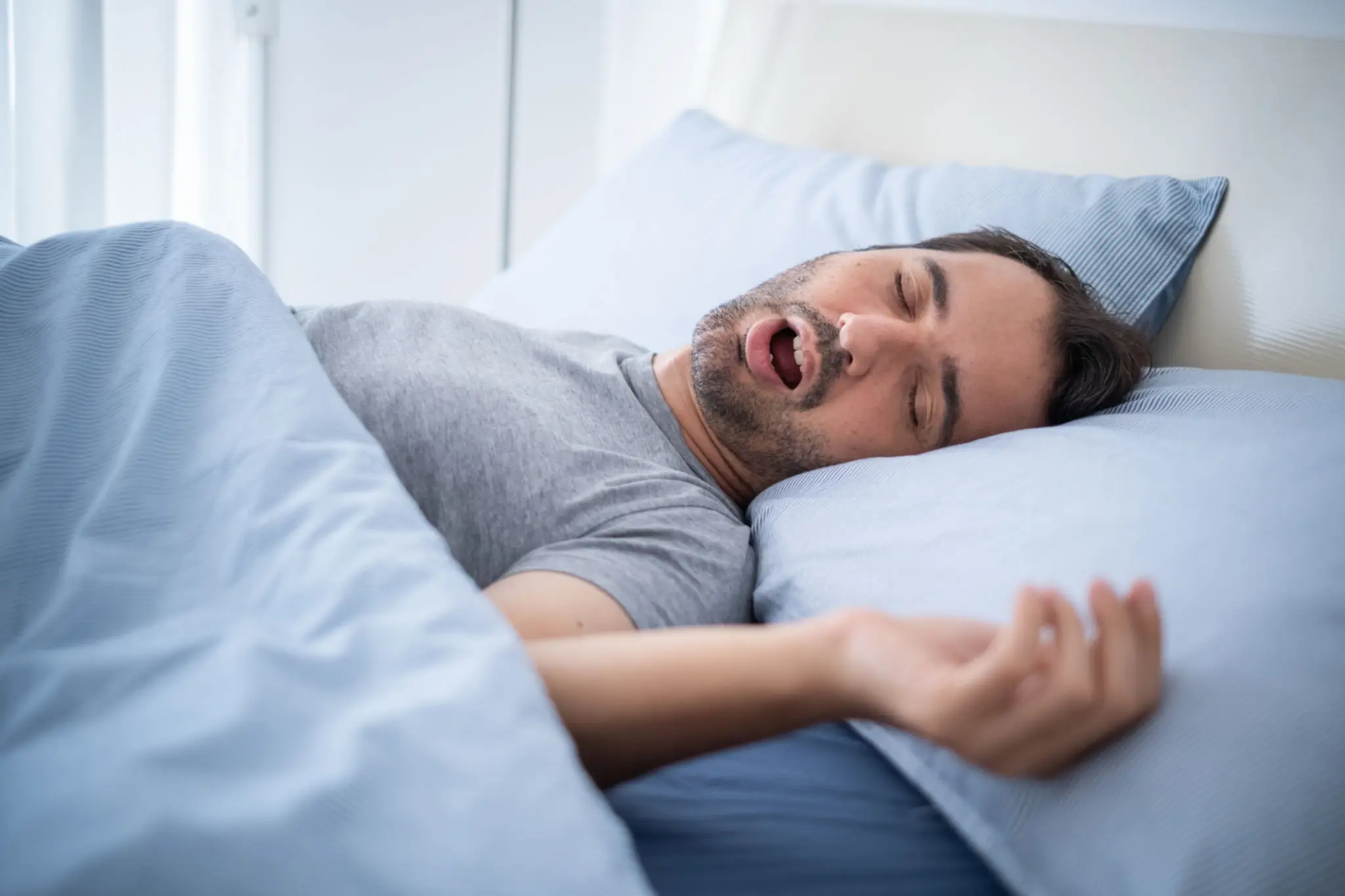 A man is sleeping in bed with his mouth open.
